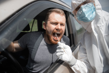 Doctor in protective virus suit taking swab from person driver to test for COVID-19 coronavirus...