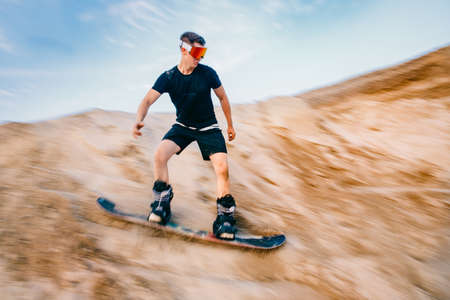 Extreme descent sand on snowboard in desert. Male snowboarder on dunesの写真素材
