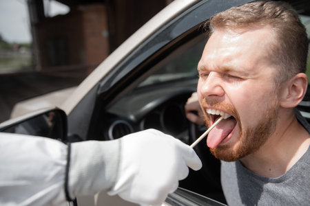 Doctor in protective virus suit taking swab from person driver to test for COVID-19 coronavirus...