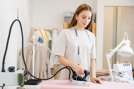 Garment steamer, woman seamstress smoothes fabric for applying patterns and sewing dressesの写真素材