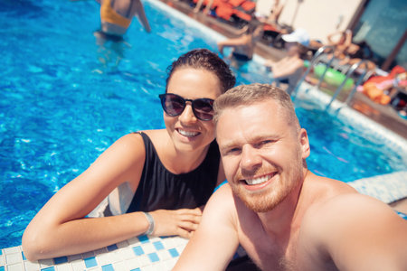 Cheerful happy couple guy and woman make selfie photo in hotel pool, summer vacation travel