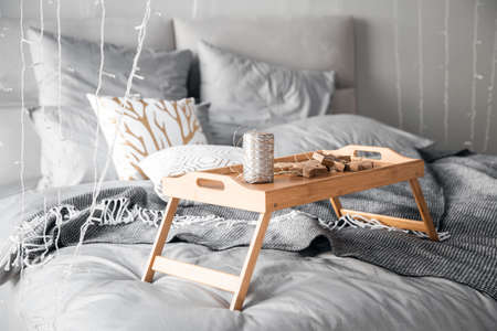 Wooden small breakfast table stands on bed in bedroom, gray sheets, sun shines through window sunriseの写真素材