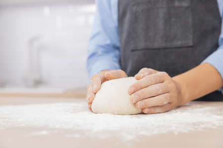 Woman hands kneading dough on board sprinkled with flour on background of light scandi kitchenの写真素材