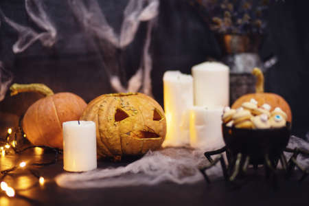 Stylized halloween sweet candies and cookies for holiday on dark background with cobwebs, pumpkins and candlesの写真素材