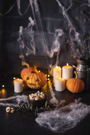 Candies and cookies in shape of an eye for holiday of halloween, dark background with cobwebs, pumpkins and candlesの写真素材