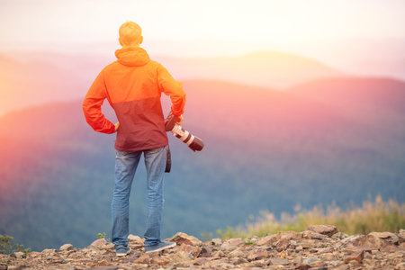 Photographer man admires sunsets, successful takes photo on travel tour with camera, back view