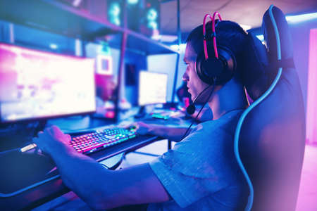 Young man gamer play online video games with headphones in internet club cafe, blue color. Esports conceptの写真素材