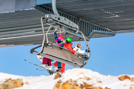 Group friends skier and snowboarders man and two women ski lift on blue sky backgroundの写真素材