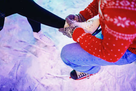 Man helps to put on skates for ice rink snow to girl, concept of winter vacation, family restの写真素材