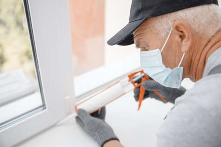 Construction worker in medical mask use gun silicone tube for repairing and installing window in houseの写真素材