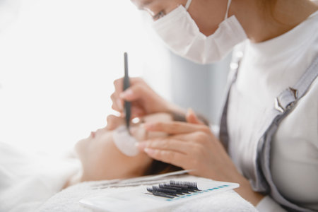 Master tweezers sets fake lashes on beautiful woman. Eyelash extension procedure