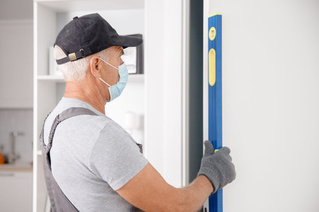 Checking doorway for verticality using bubble level by master carpenter wearing medical mask