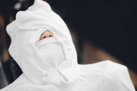 Man sits in barbershop chair and steam his face with hot towel in front of royal beard shaving razorの写真素材