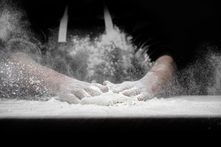 Hands of male baker preparing yeast dough with white flour dust on black background, scoop out for...