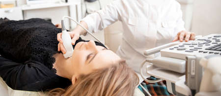 Doctor conducts ultrasound examination of woman thyroid gland in clinic, lack of iodineの写真素材