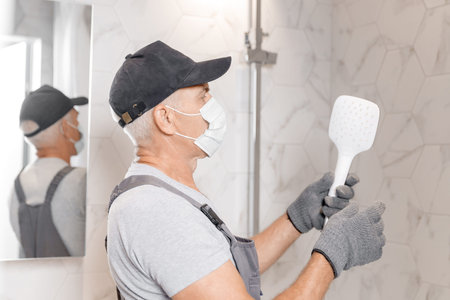 Plumber in medical mask installing shower stall, work in bathroomの写真素材