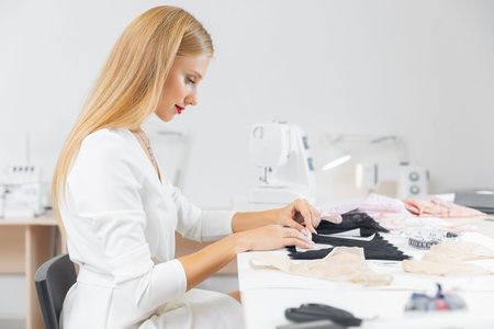Workplace of seamstress tailor. Young female designer cuts out pattern of fabric from sketch line...