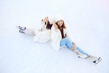 Lifestyle portrait of two friends happy young woman in white hat and coat in skates on winter ice...