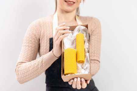 Master woman artisan in apron holds packaged finished product yellow candles made of bees wax with...