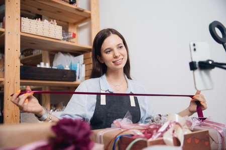 Online tutorial gift wrapping, young woman records Internet video on phoneの写真素材