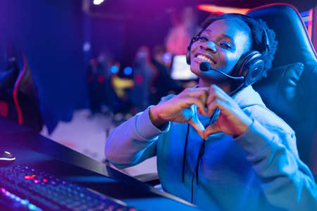 Streamer African beautiful girl shows heart sign with hands professional gamer playing online games computer, neon colorの写真素材
