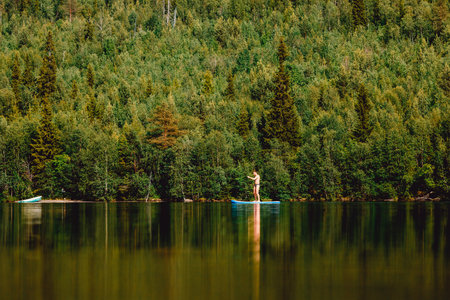 Man rowing oar on sup board blue lake water paddleboard background of forestの写真素材