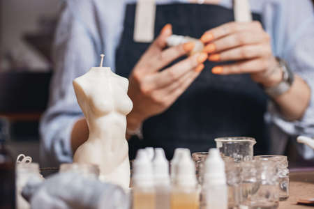 Beautiful young woman workplace is engaged in production of aromatic wax candles in shape of female Venus body. Concept craftswoman small businessの写真素材