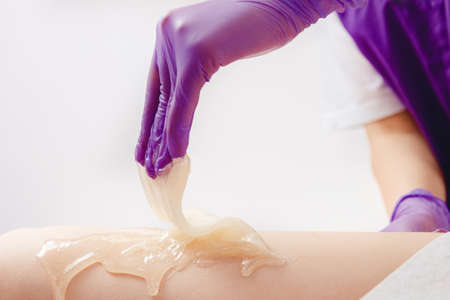 Shugaring hair removal concept. Process depilation of legs girl with sugar paste in spa salon, white backgroundの写真素材