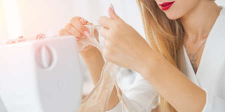 Woman fashion designer sews underwear, holds beige panties made of mesh in handsの写真素材