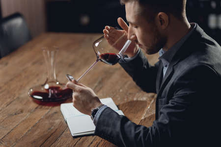 Sommelier compiles tasting card of alcohol for restaurant, evaluates red wine in glassの写真素材