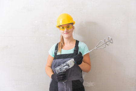Woman independently makes repairs in new house, holds mixer for mixing plaster on walls
