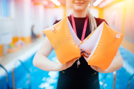 Swimming school for children, woman trainer holds inflatable armbands for kids accessories