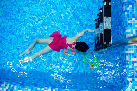 Kid little girl learning to underwater swim pool with ring with coach woman