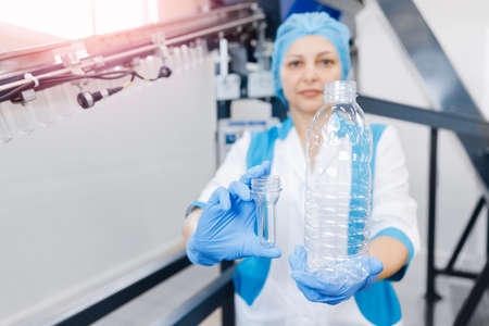 Woman worker holds converting plastic preform blank into pet bottle for drink beverage filling in food industryの写真素材