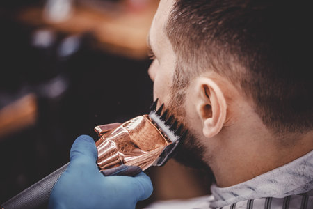 Close-up of barber with medical gloves shearing beard to man in barbershop. Haircut coronavirus...