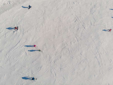 Snowboarders and skiers drive down ski slope in winter through fresh snow, areal top viewの写真素材