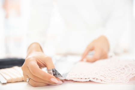 hands of a woman seamstress measure the length of the lace with a tape for sewing underwearの写真素材