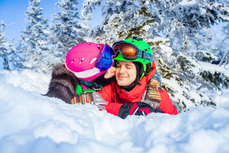 Snowboarder man and woman skier hugging and having fun on background of winter forest and snow. Sunlight in mountainsの写真素材
