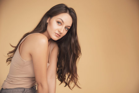 Beautiful portrait of Caucasian young brunette woman with brown eyes on beige background in studio....