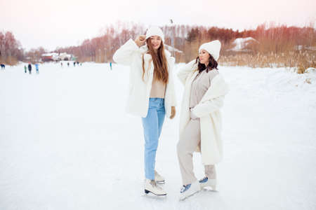 Young happy women in winter with skates on open air ice rink. Girl friendship conceptの写真素材