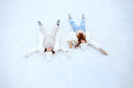 Lifestyle portrait of two friends happy young woman in white hat and coat in skates on winter ice rink, top viewの写真素材