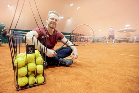 Smiling man tennis trainer player with racket and ball on courtの写真素材