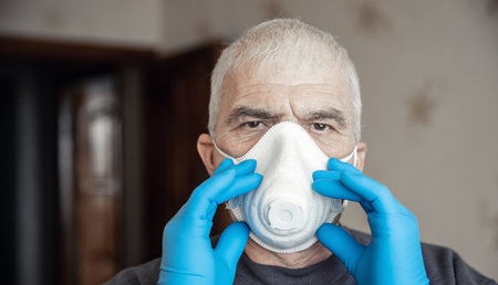 White protective mask tired eyes of old senior male doctor after hard shift in covid hospitalの写真素材