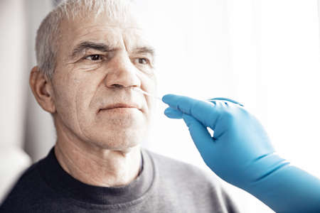 Medical worker wearing protective equipment testing senior old man for dangerous corona virus using test swab stickの写真素材