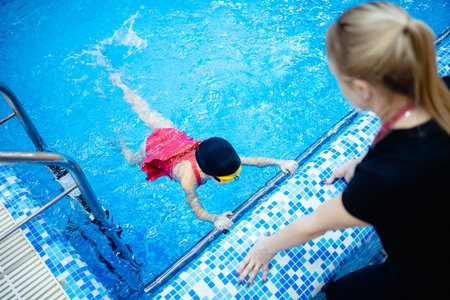 Team woman coach and kid athlete in pool, swimming training school for childrenの写真素材