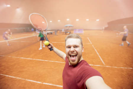 Smiling young man player tennis prepares to serve ball during match courtの写真素材