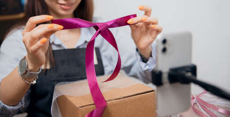 Gift box wrapping, young woman records Internet video tutorial on phoneの写真素材