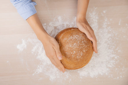 Baker hand wheaten Round loaf of bread lies on table with flour, white kitchen background top view