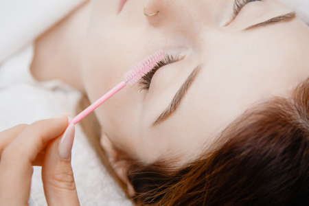 Eyelash extension procedure. Woman master combs lashes fakeの写真素材