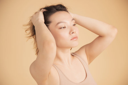 Profile young girl of Asian appearance with wavy streaked hair on beige background. Concept beauty...